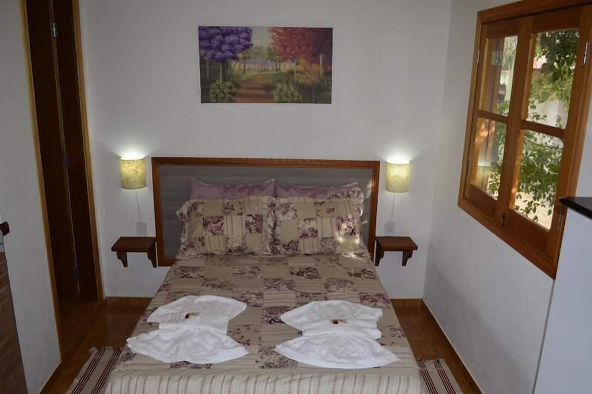 Ein Schlafzimmer mit einem hölzernen Kopfteil, zwei Nachttischlampen, einer blumigen Bettdecke und einem Gemälde über dem Bett.