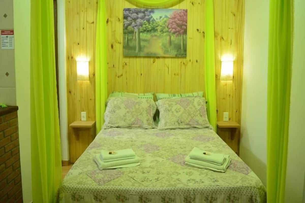 Ein Bett mit blumigem Überwurf, zwei Kissen und zwei gefaltete Handtücher an einem hölzernen Kopfteil, über dem ein Gemälde hängt.