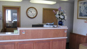 A reception area with a wooden desk, a clock, a vase of flowers, and a painting on the wall. - Crown Inn (Seattle)