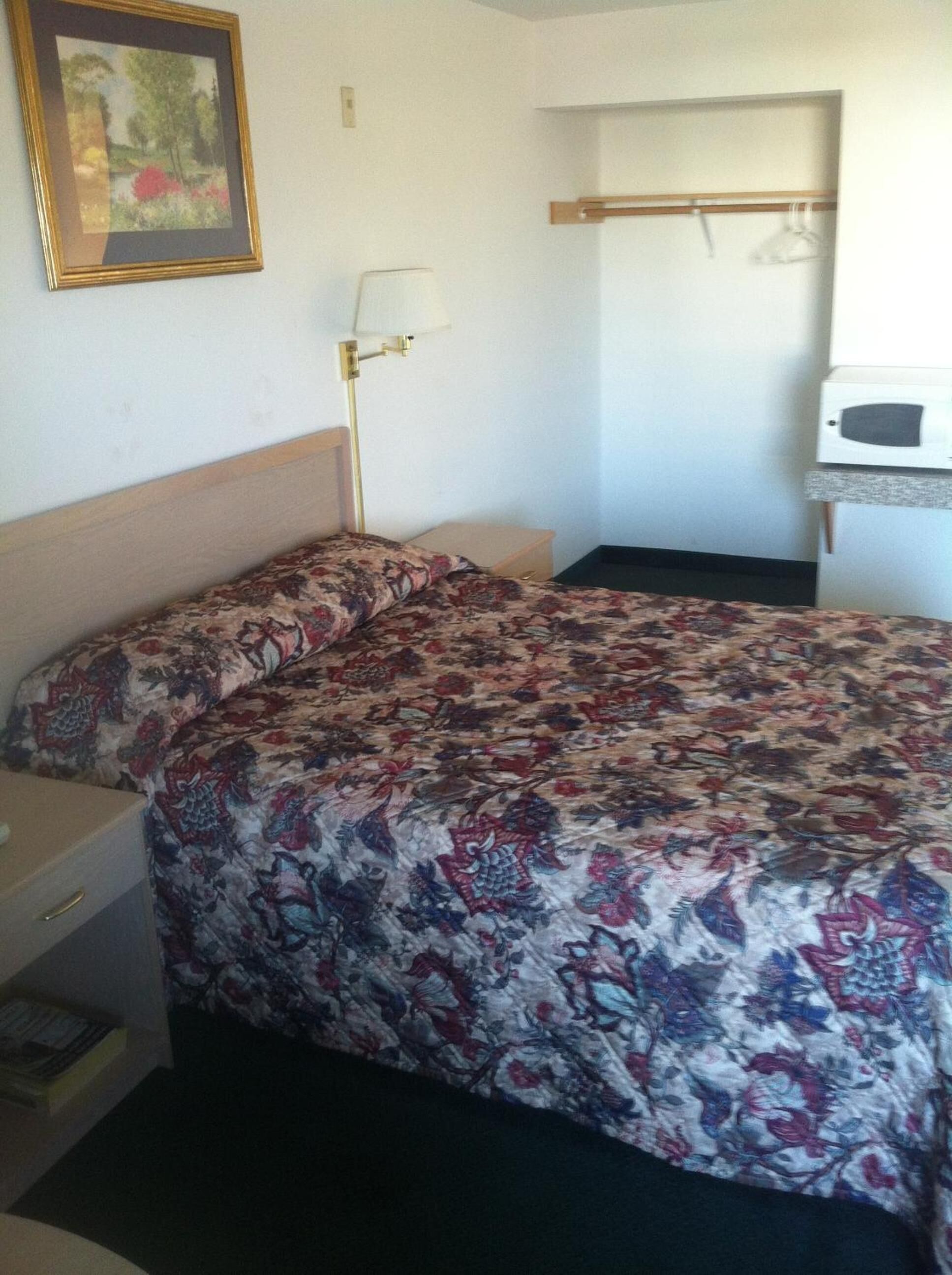 Une chambre à coucher avec un lit, une table de chevet, une lampe, une armoire et un tableau encadré au mur.
