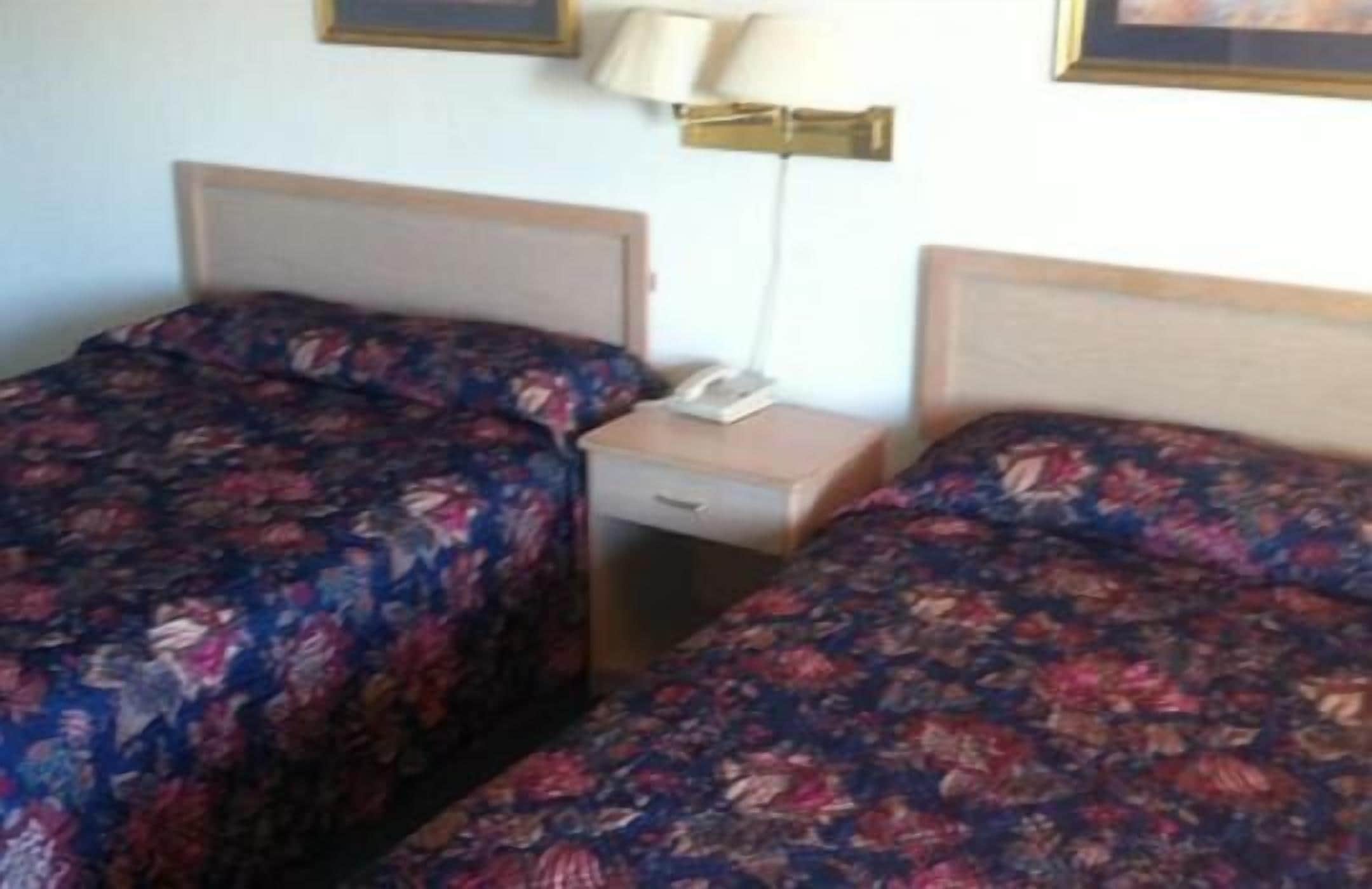A hotel room with two single beds, a bedside table with a lamp, and a phone.