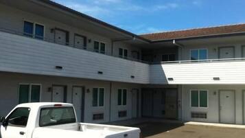 Un motel de dos pisos con fachada blanca, numerosas ventanas y un estacionamiento con una camioneta pickup blanca.