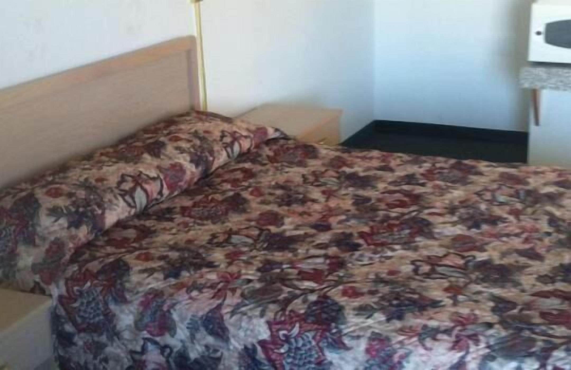 A single bed with a floral-patterned bedspread, a wooden headboard, and a bedside table with a lamp.