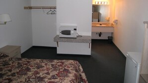 A hotel room with a bed, a microwave on a small table, a sink with a mirror, and a lighted vanity area. - Crown Inn (Seattle)