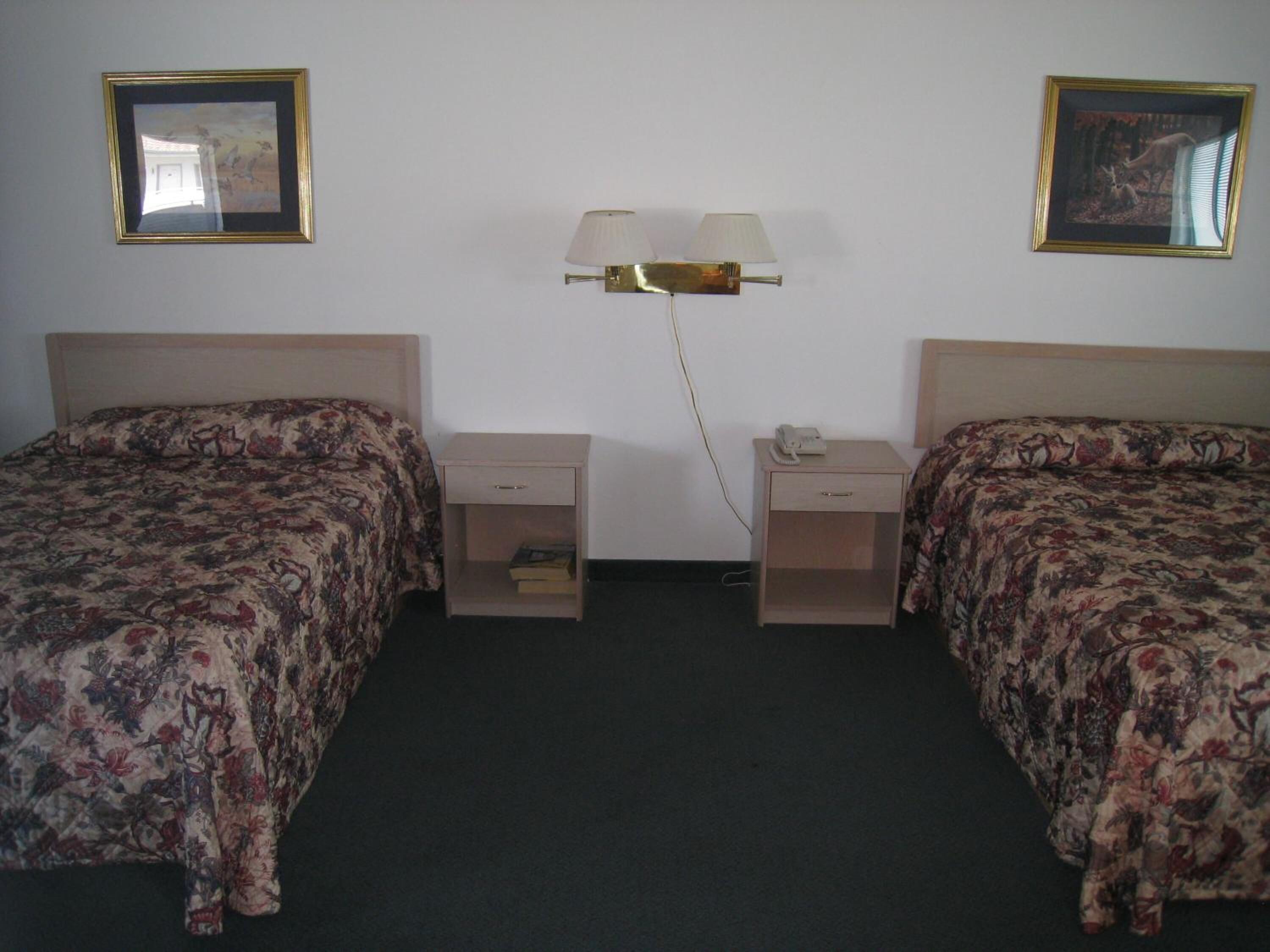 Una habitación de hotel con dos camas, una mesita de noche con un teléfono y una lámpara de pared.