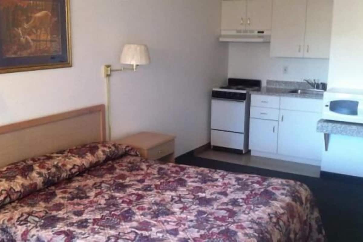 A hotel room with a bed, a small bedside table, a lamp, a kitchenette with a microwave, and a cabinet.