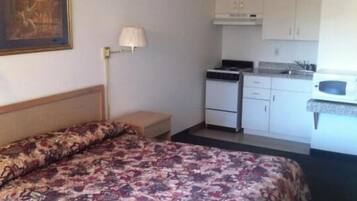 Une chambre d’hôtel comprenant un lit, une petite table de chevet, une lampe, une kitchenette équipée d’un four à micro-ondes et un placard.