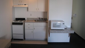 A compact kitchen with white cabinets, a stove, a sink, and a microwave. - Crown Inn (Seattle)