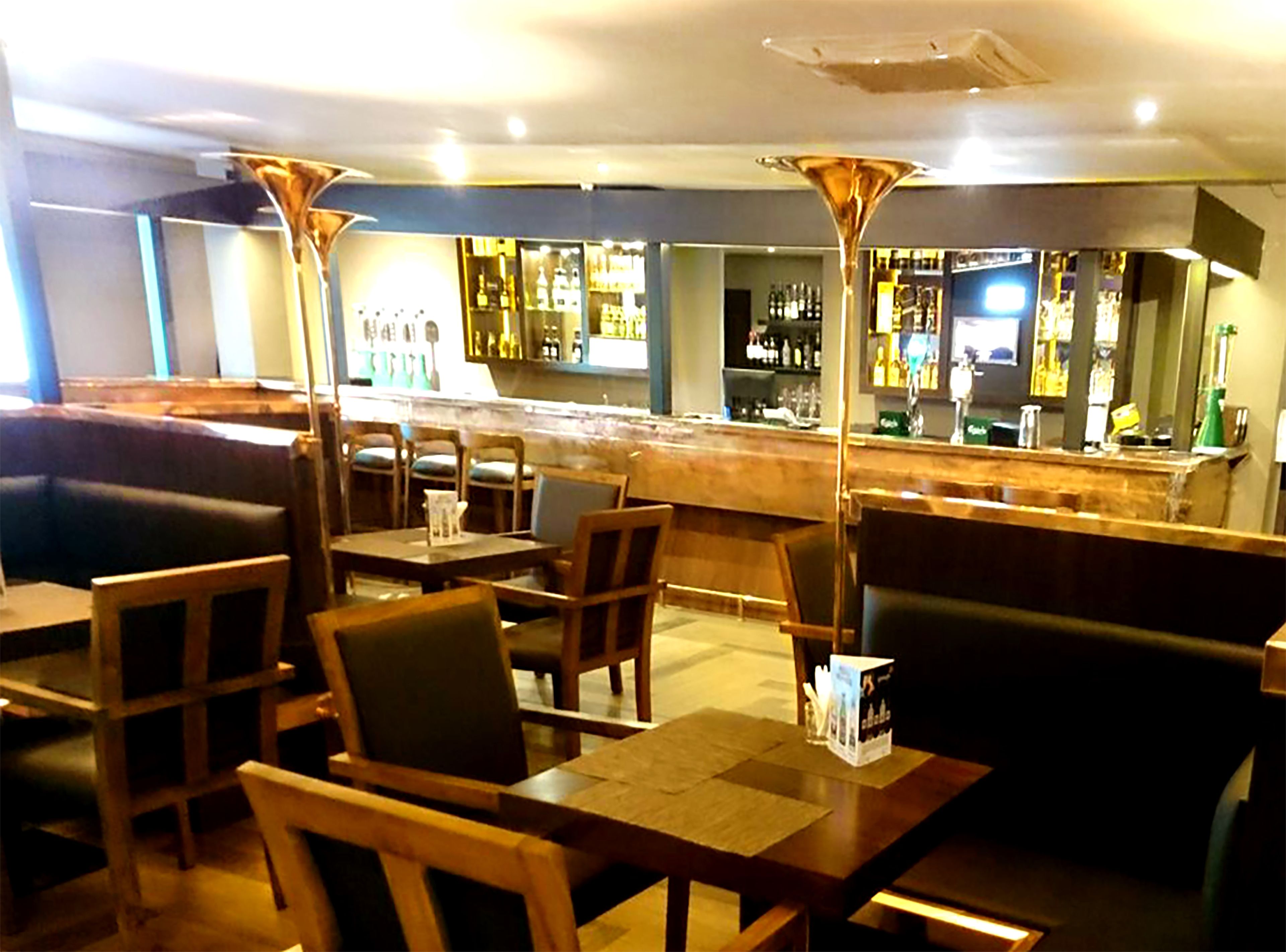 A bar area with wooden tables and chairs, a counter with bottles, and a seating area with cushioned benches.