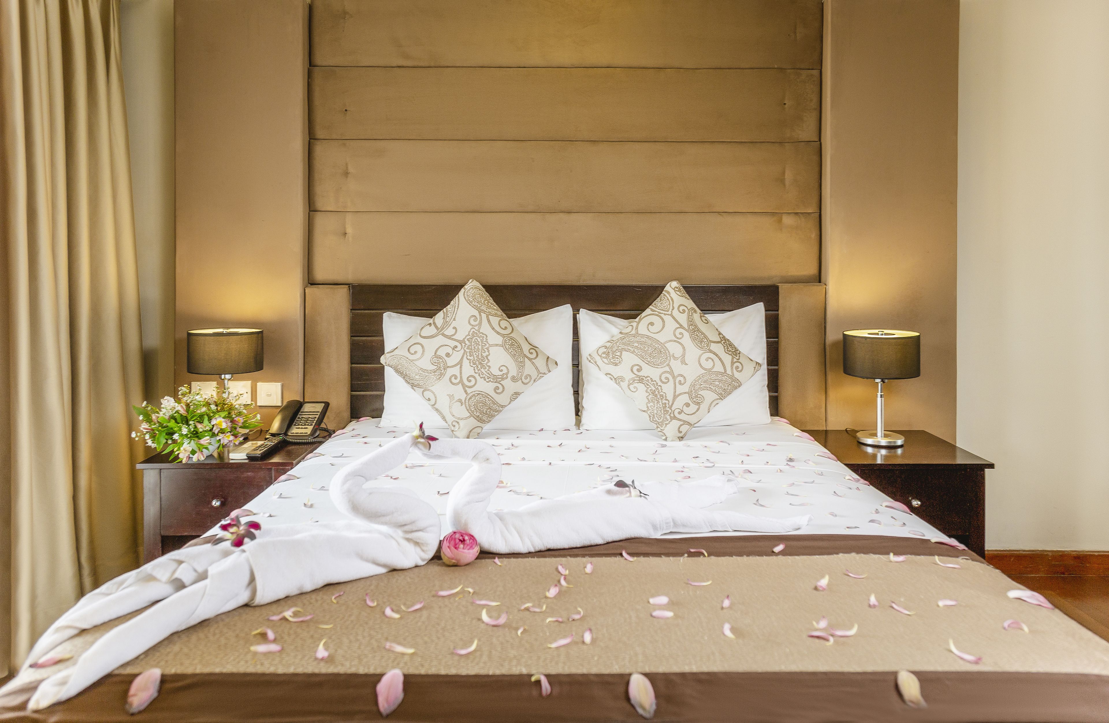 Hotelkamer met een groot bed, twee nachtkastjes, een lamp, een telefoon en een bloemenarrangement.