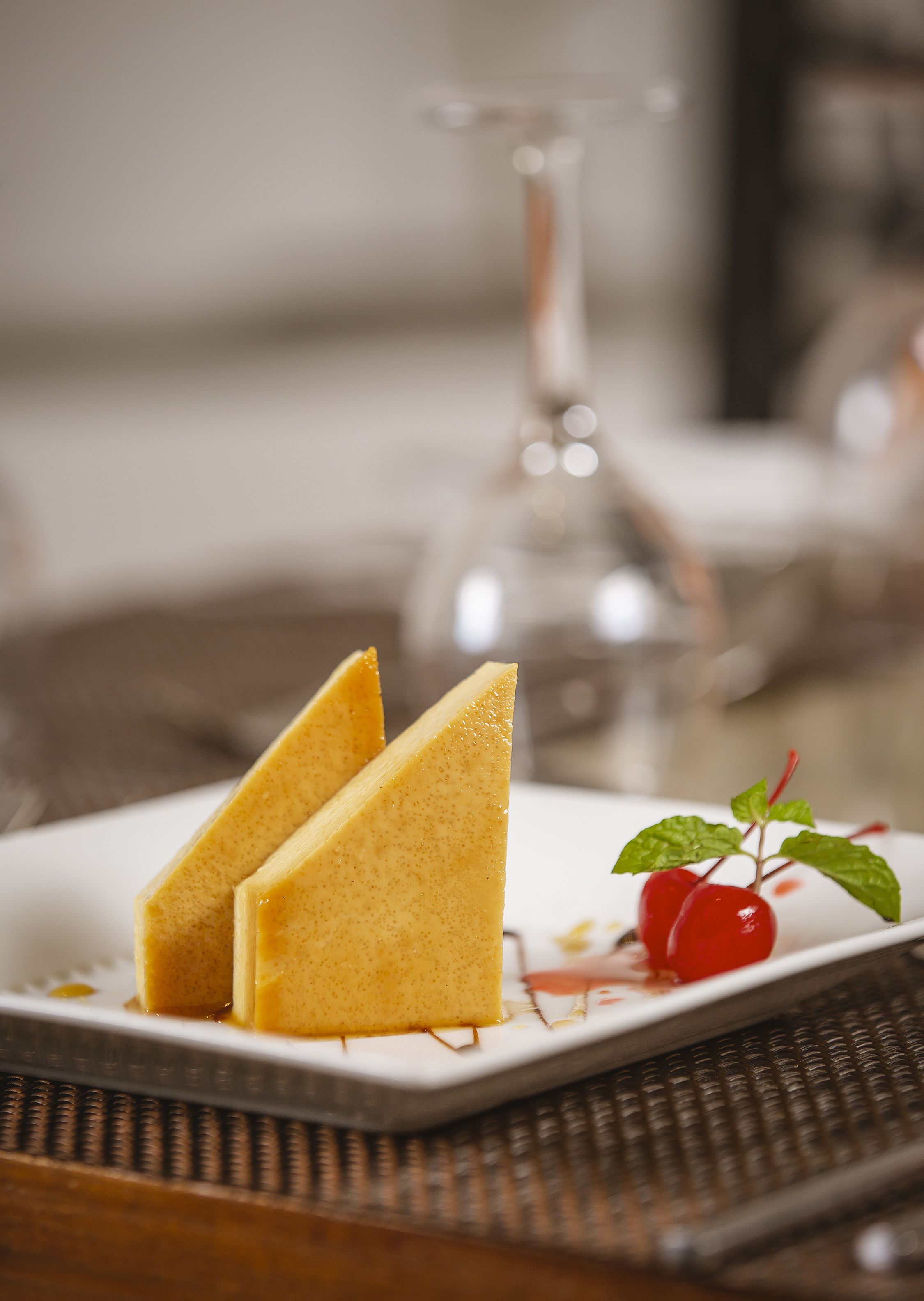 A dessert plate with two triangular slices of cake, a cherry, and a mint leaf on a white plate.