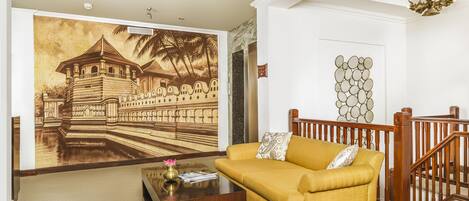 Una sala de estar con un mural grande en la pared, un sofá amarillo, una mesa de centro de madera y una escalera.