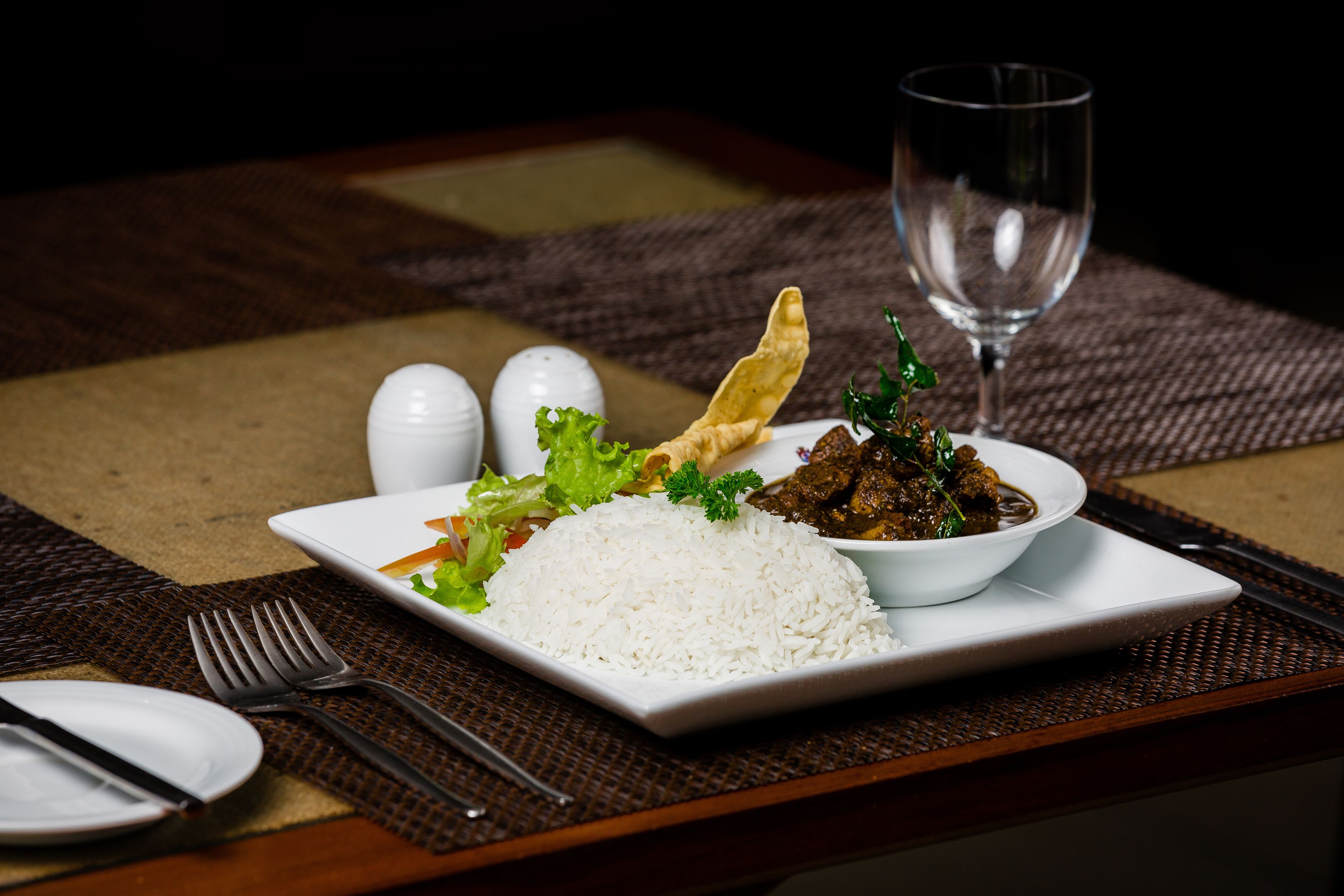 A dining table with a plate of white rice, a bowl of meat dish, and a glass of water.