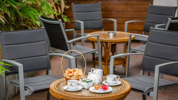 Una mesa de mimbre con un juego de té, una cesta de pasteles y un cuenco pequeño de mermelada.