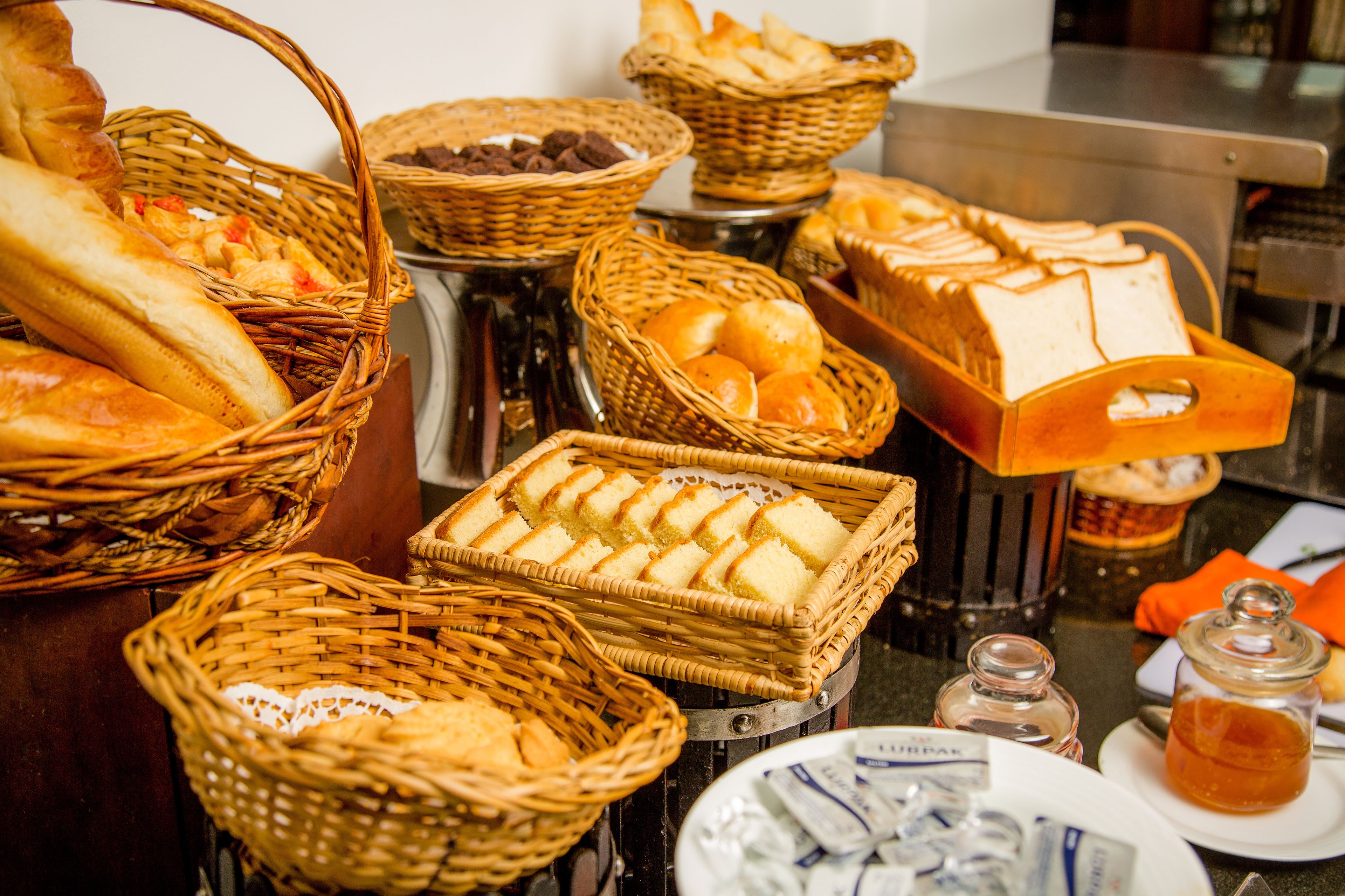 A variety of breads and pastries displayed in baskets and on a tray, suggesting a bakery or breakfast setting.
