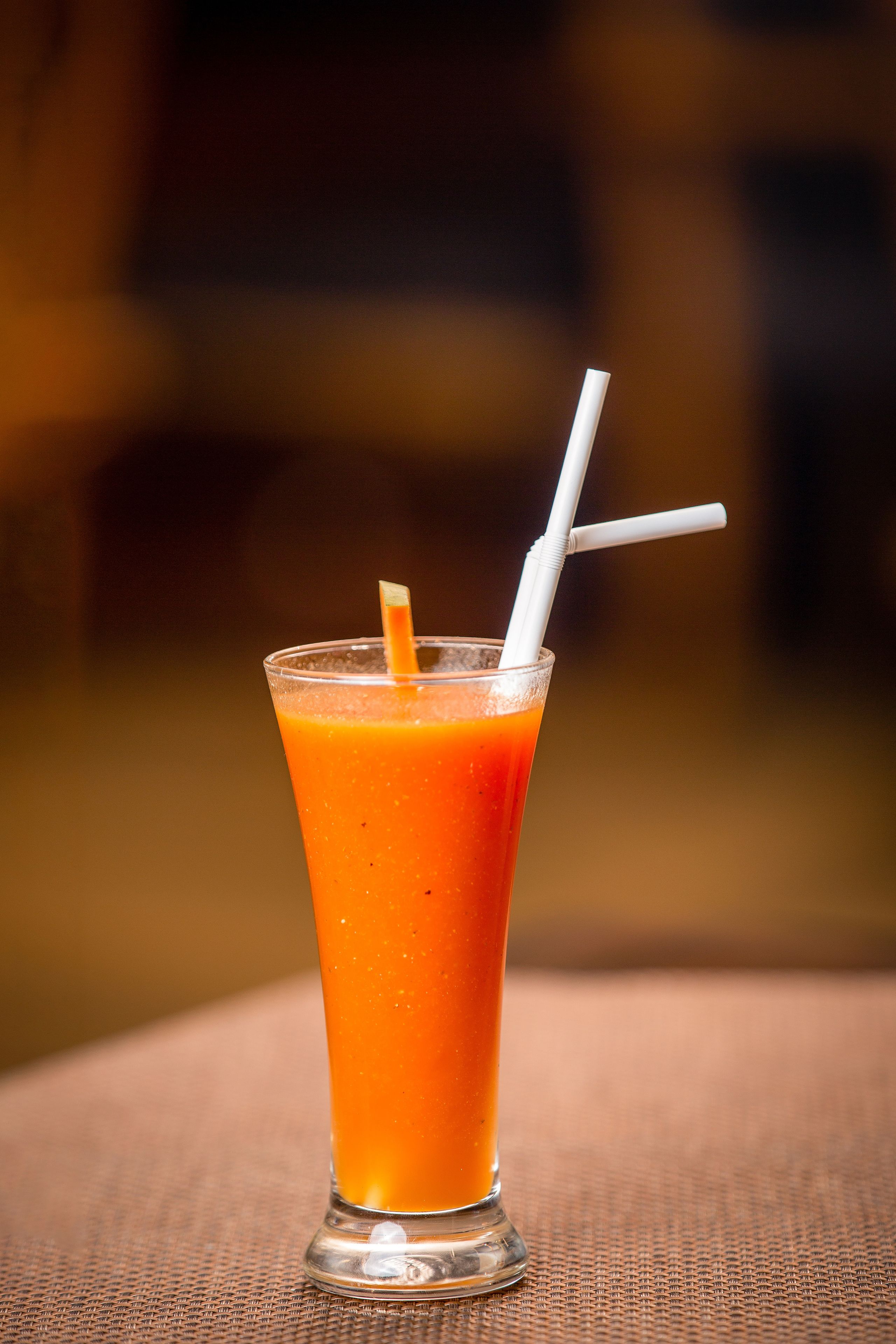 A tall glass with a straw, filled with a red-orange liquid, placed on a textured surface.
