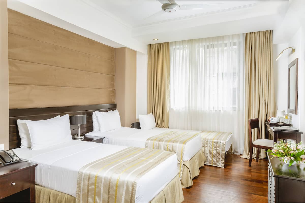 A hotel room with two beds, a wooden headboard, a desk with a chair, a telephone, and a window with curtains.