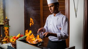 Un chef cocina entre llamas, rodeado de verduras y un farol decorativo.