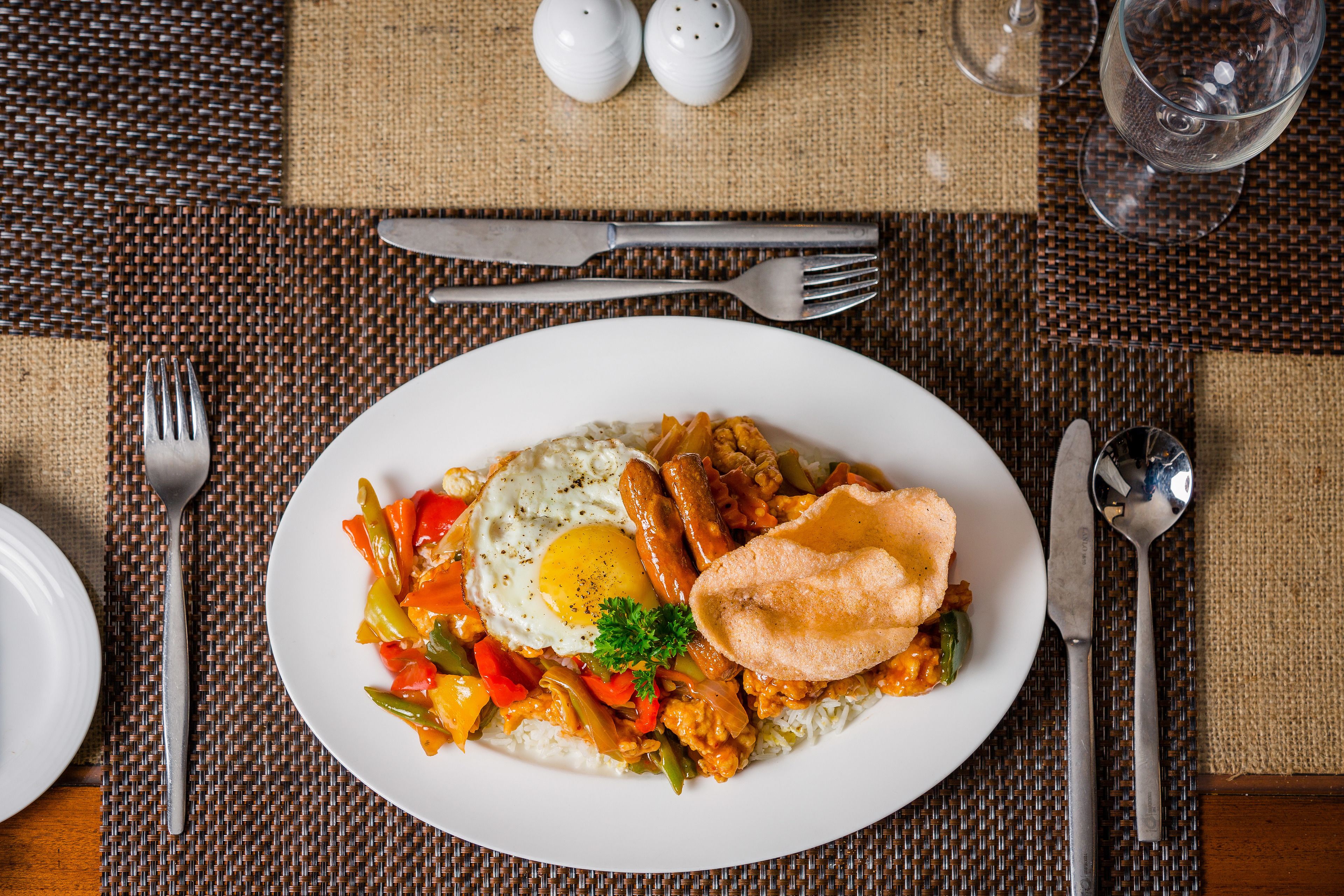 Un plato de comida con un huevo frito, salchichas y verduras sobre un posavasos tejido.
