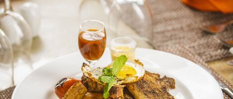 A plate of grilled vegetables and a small glass of sauce on a table with a placemat.