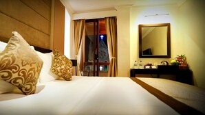Habitación de hotel con cama, mesita de noche, espejo y vista a la aguja de una iglesia por la ventana.