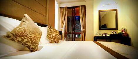 Habitación de hotel con cama, mesita de noche, espejo y vista a la aguja de una iglesia por la ventana.