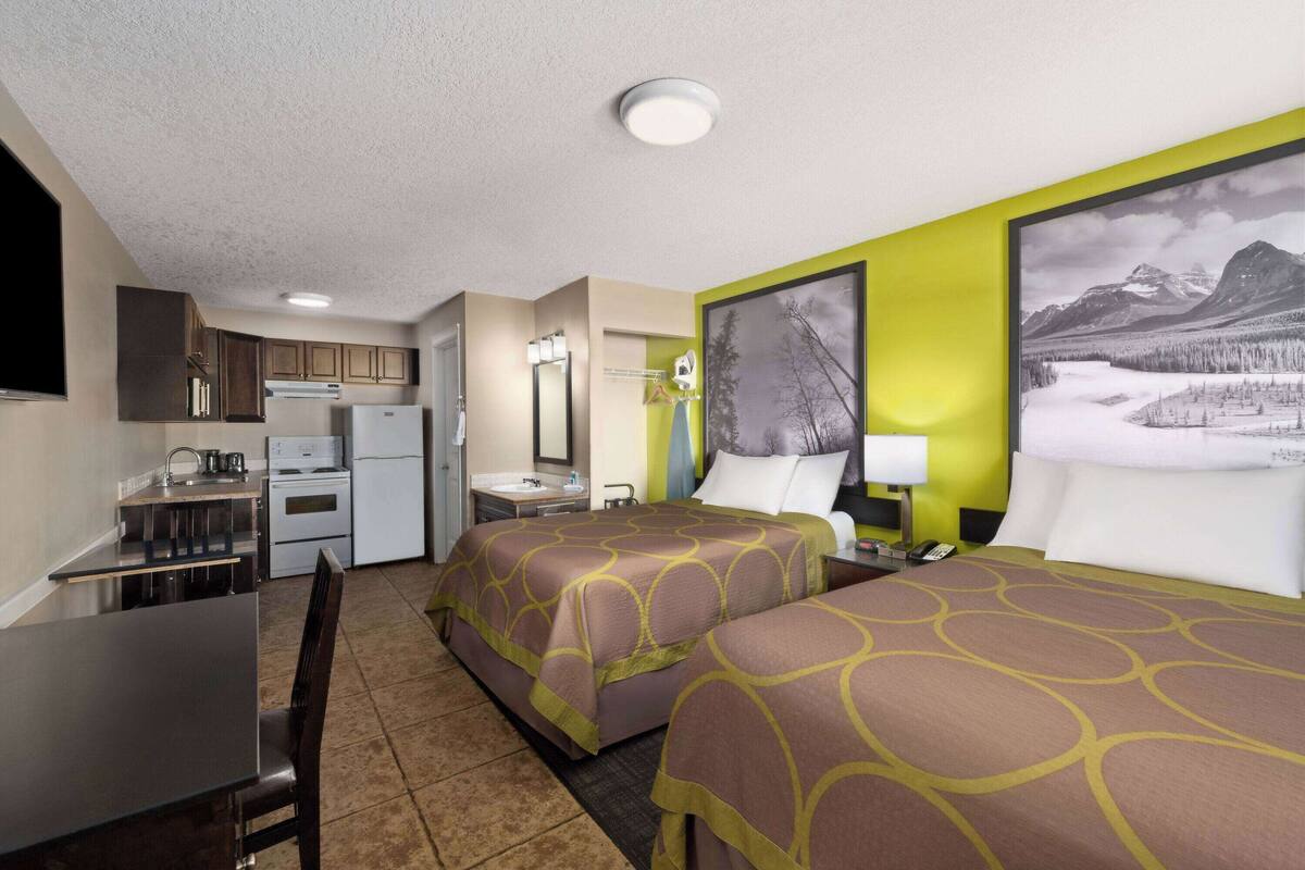 A hotel room with two beds, a kitchenette, a bathroom, and a large window with a mountain view.
