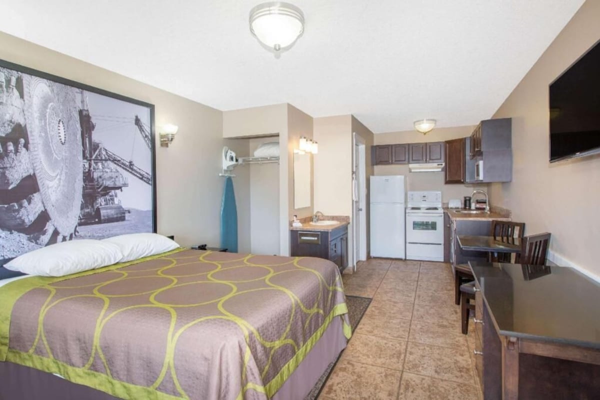 Un dormitorio con cama, una kitchenette con refrigerador, estufa y microondas, y una zona de comedor con mesa y sillas.
