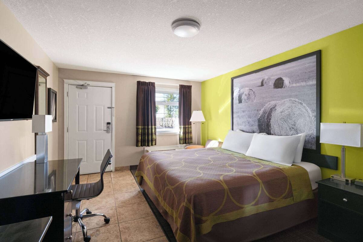 A hotel room with a bed, a desk, a chair, a TV, and a window with curtains.