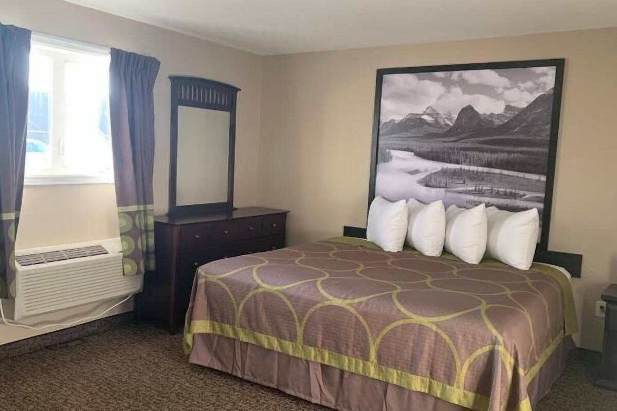 A hotel room with a bed, a dresser, a mirror, a window with curtains, and a wall-mounted air conditioner.