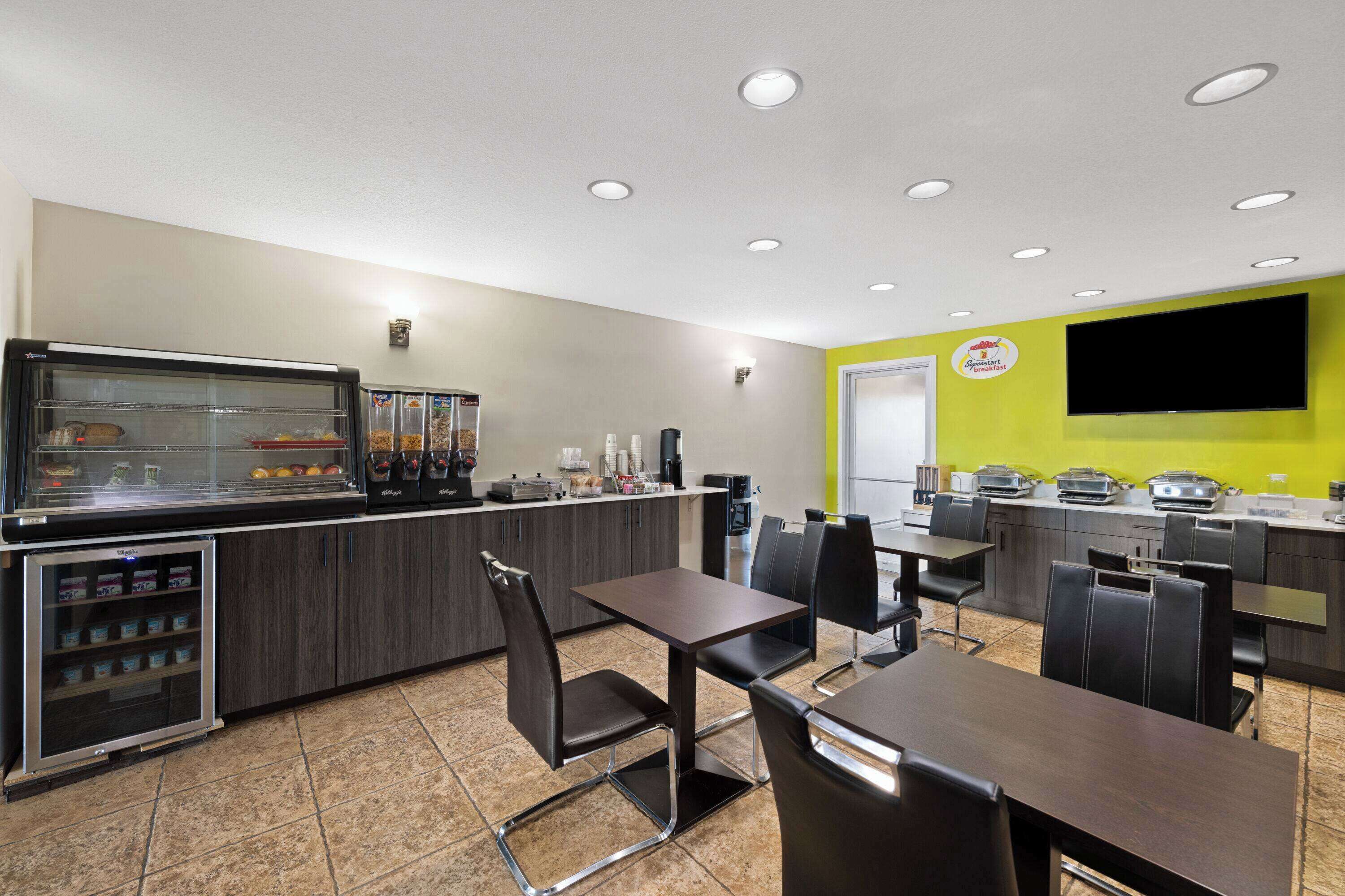 Una cafetería moderna con un mostrador de autoservicio, una zona de estar y un televisor de pantalla plana grande en la pared.