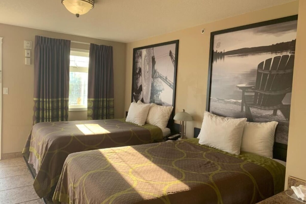 Habitación de hotel con dos camas, una ventana con cortinas, y una obra de arte que muestra un puente y un barco.