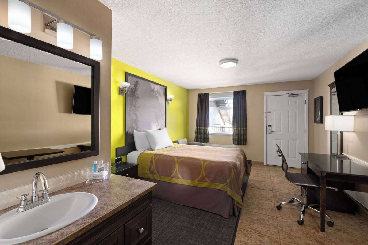 A hotel room with a bed, a desk, a chair, a sink, and a mirror.