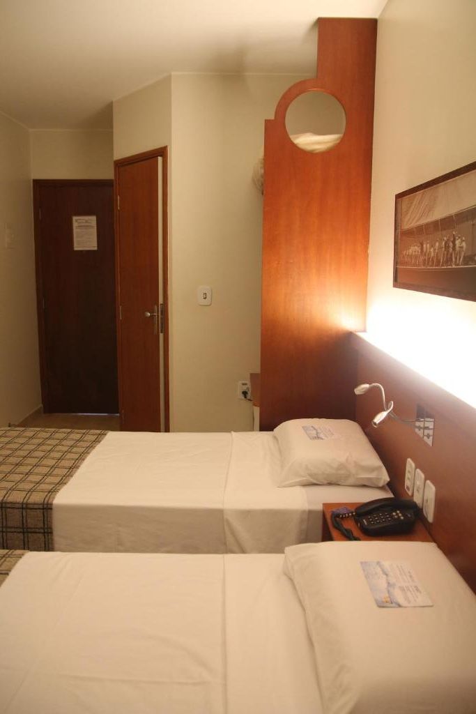 Habitación de hotel con dos camas individuales, cabecera de madera, teléfono montado en la pared y puerta que da a otra habitación.