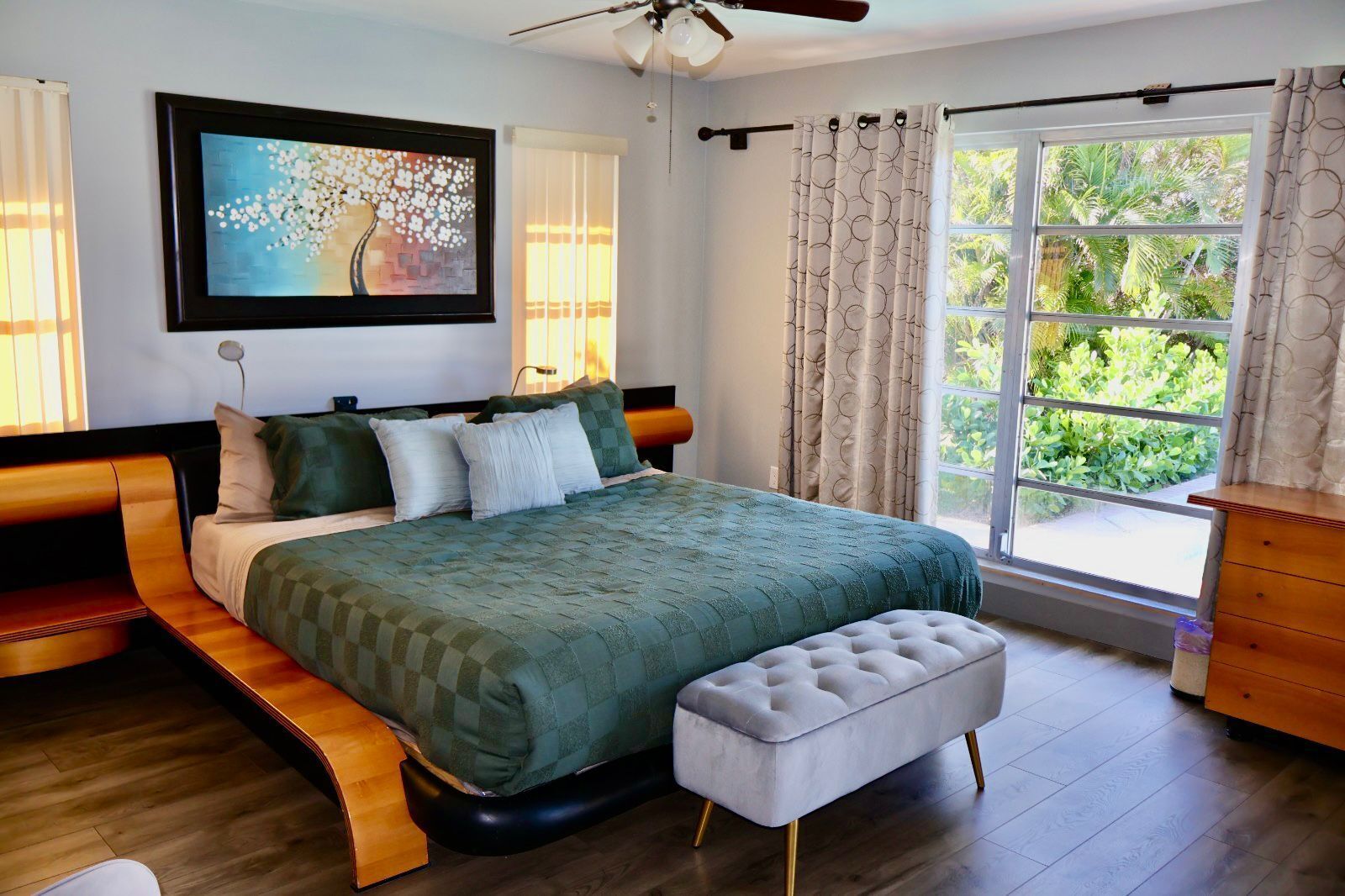 A bedroom with a bed, a bench, a dresser, a ceiling fan, and a window with curtains.