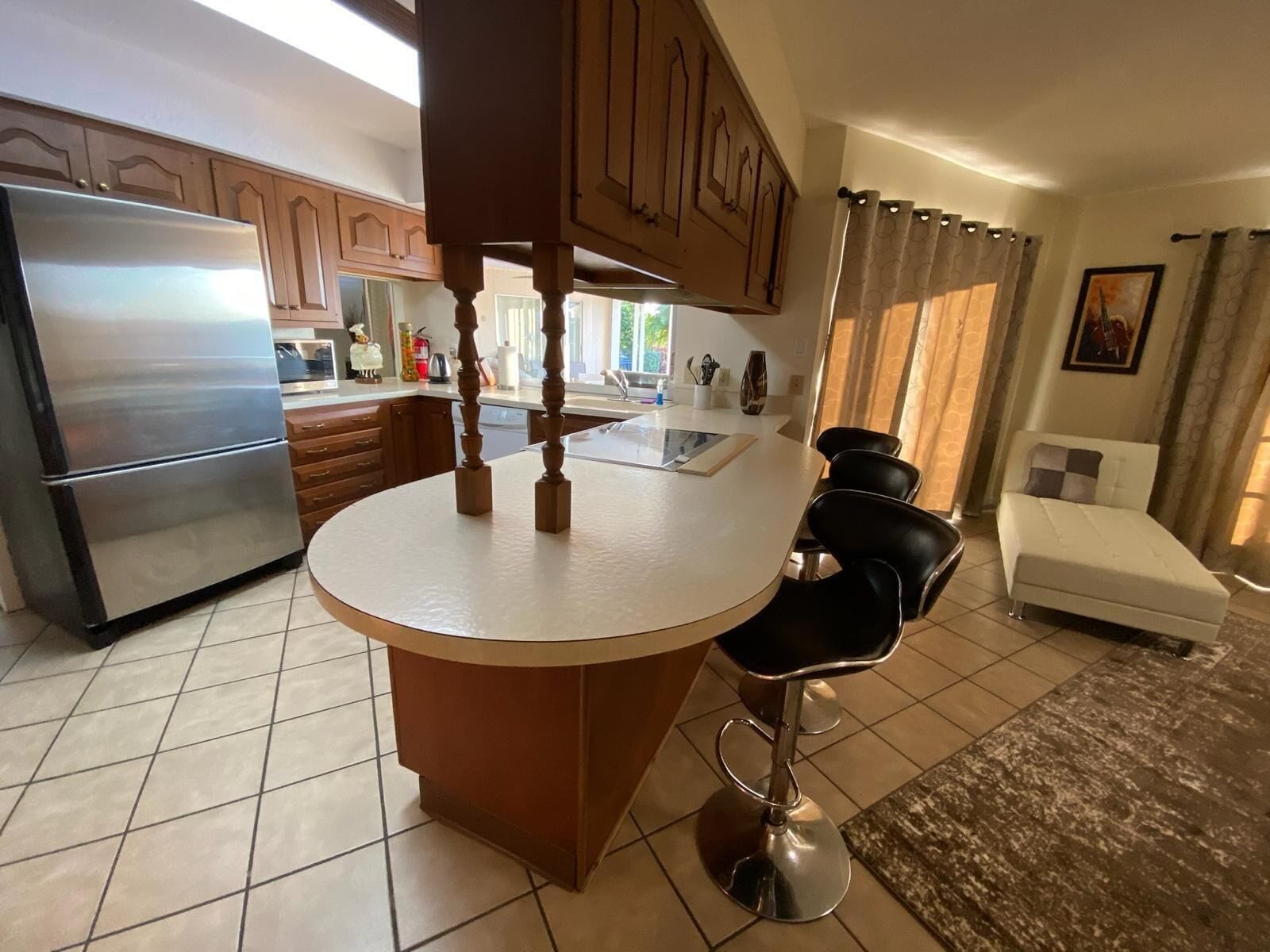 Een keuken met een centraal eiland, een koelkast, houten kasten en een zithoek met een bank en stoelen.