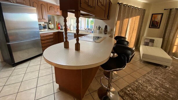 A kitchen with a central island, a refrigerator, wooden cabinets, and a dining area with a sofa and chairs. - Villa Marco Island (Marco Island)