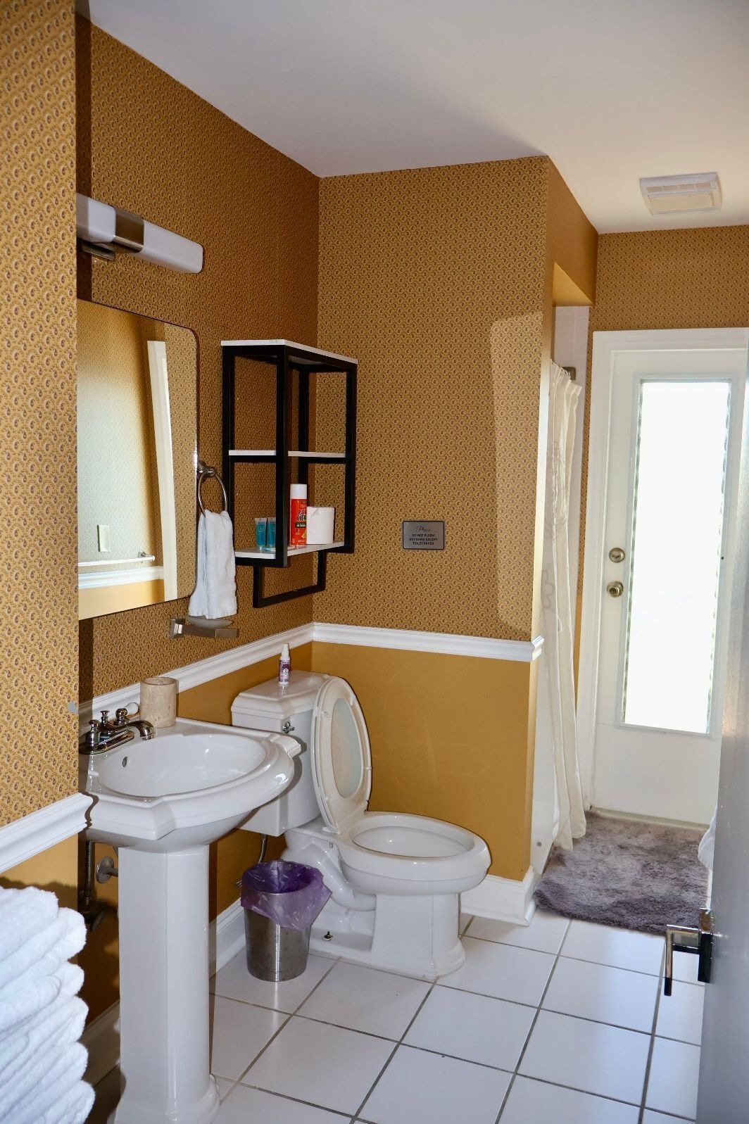 A bathroom with a toilet, sink, and mirror. There is a towel rack and a shower curtain.