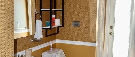 A bathroom with a toilet, sink, and mirror. There is a towel rack and a shower curtain.