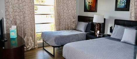 Une chambre d’hôtel avec deux lits, un bureau, une table de chevet et une fenêtre avec des rideaux.