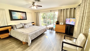 A bedroom with a bed, a desk, a chair, a TV, and a window with curtains.