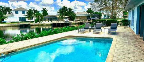 A swimming pool with lounge chairs, a dock, and a calm water body in the background.