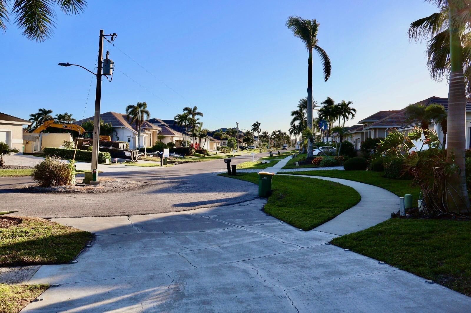 A residential street with houses, palm trees, and a sidewalk.