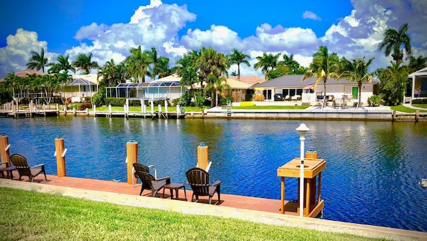 A waterfront hotel with a pool, outdoor seating, and palm trees.
