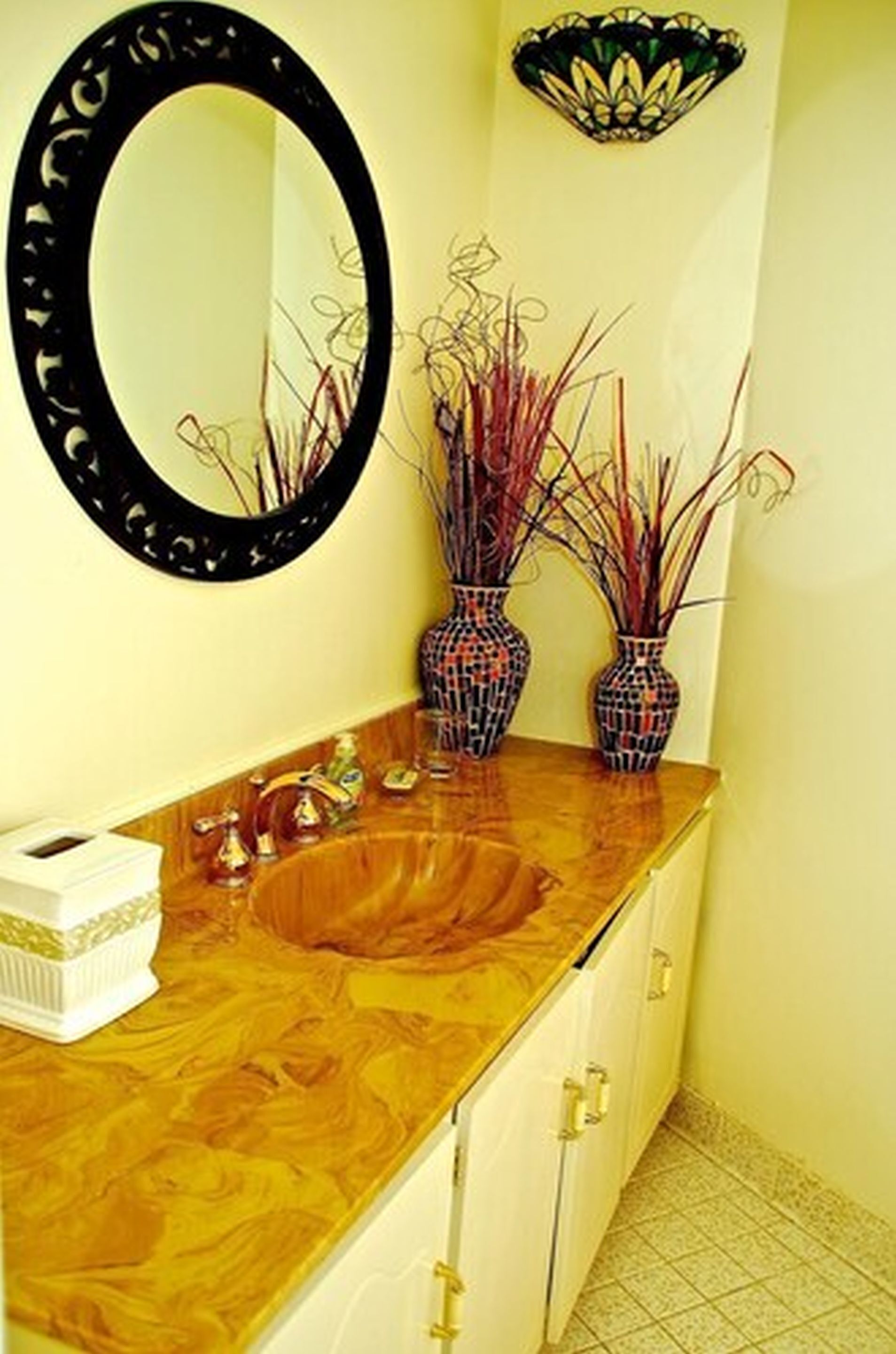 A bathroom with a wooden vanity, a round mirror, two patterned vases, and a decorative wall piece.
