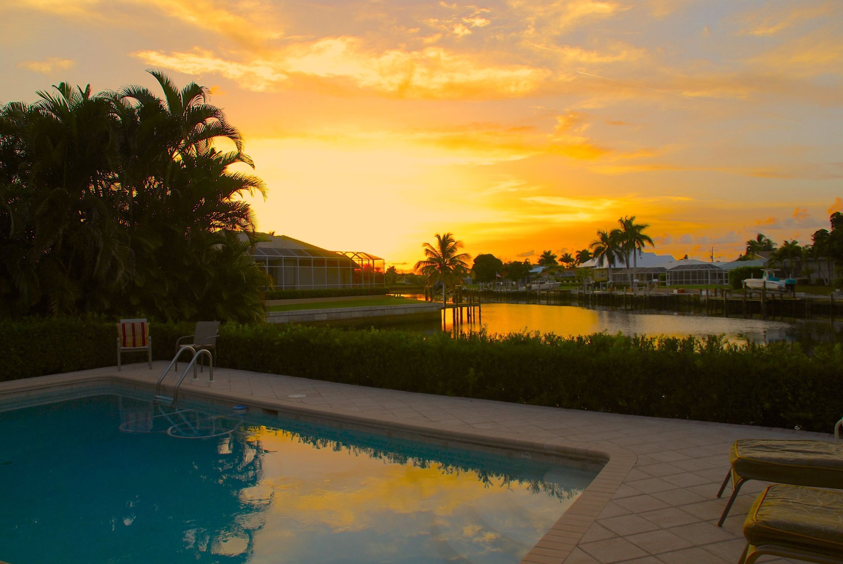 A swimming pool with a view of a sunset, palm trees, and a distant building.