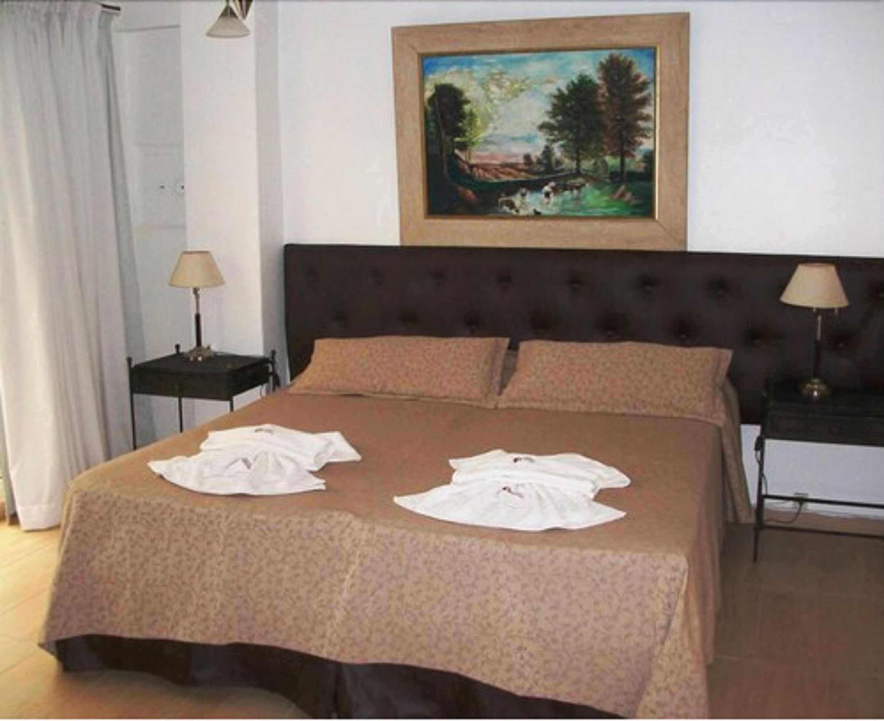 Habitación de hotel con una cama grande, dos mesitas de noche, un cuadro en la pared y una ventana con cortinas.