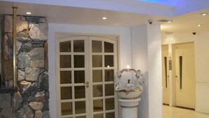 Een gang met een stenen muur, een witte deur met ruitpanelen en een wit voetstuk met gouden sierlijst.