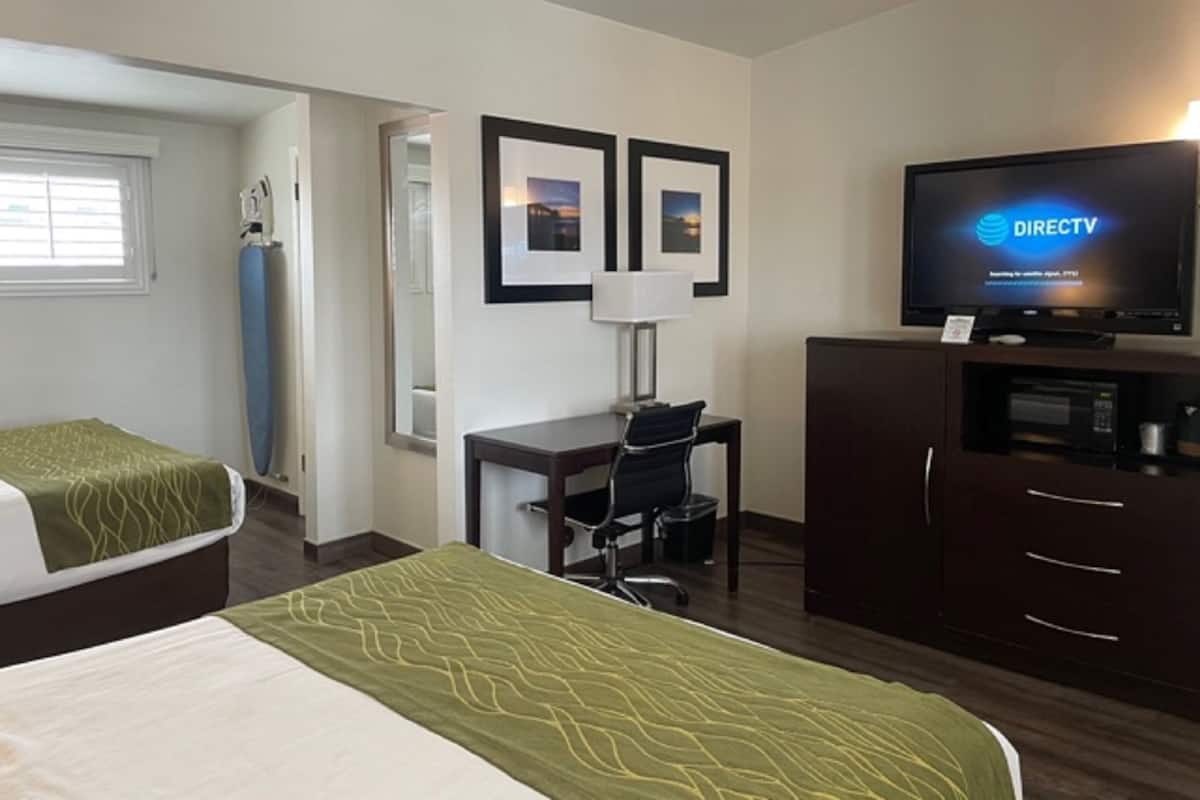 A hotel room with two beds, a desk with a chair, a television, and framed pictures on the wall.