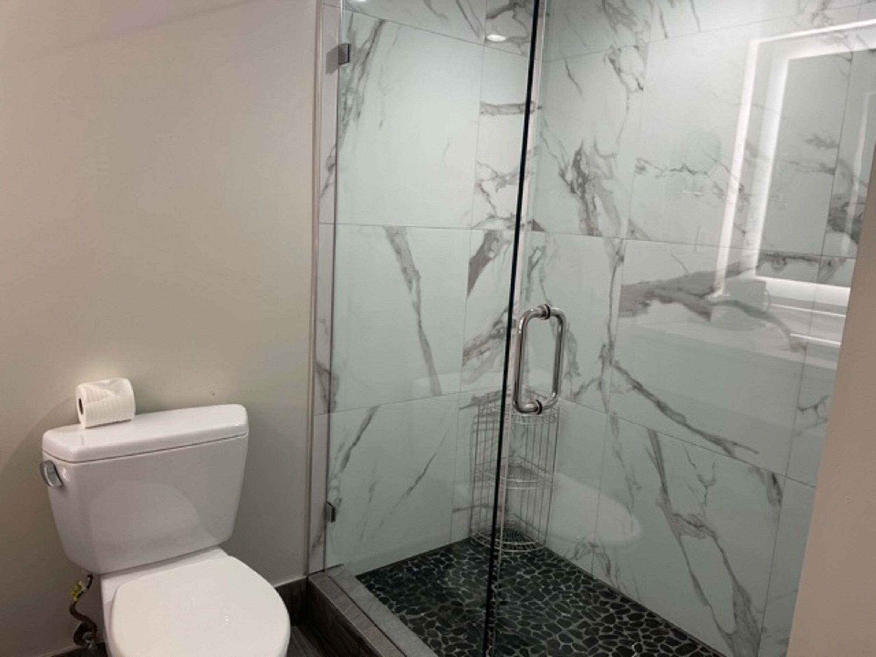 Et moderne badeværelse med bruseniche i glas, marmorfliser og et hvidt toilet.